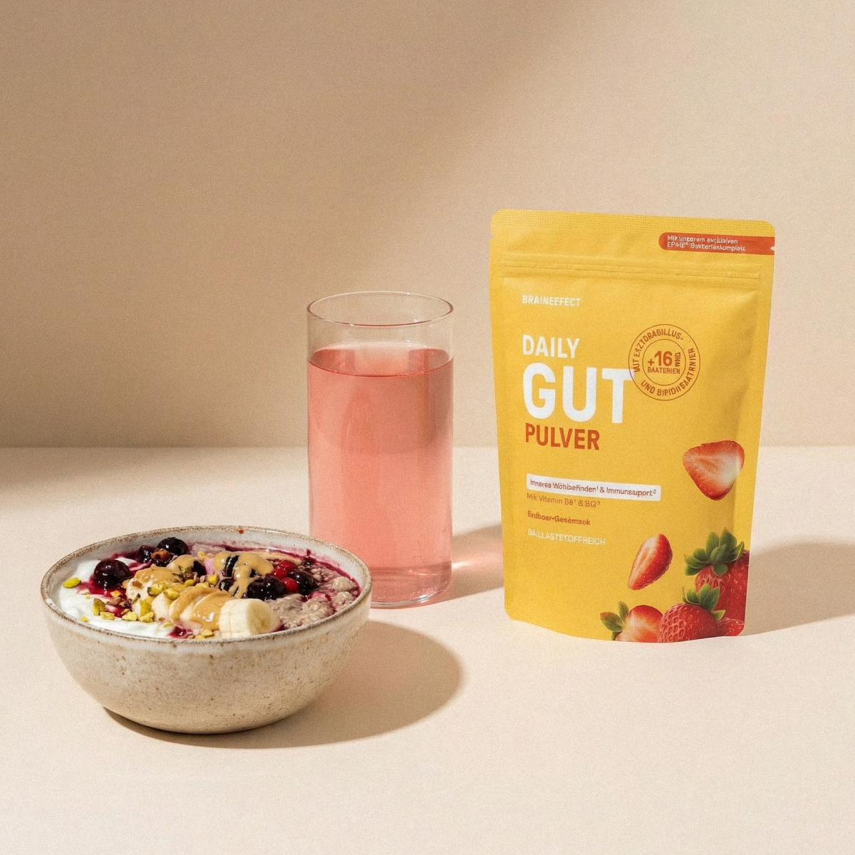 BRAINEFFECT Beutel "DAILY GUT PULVER" mit Erdbeeren neben einer Müslischüssel und einem rosa Getränk.