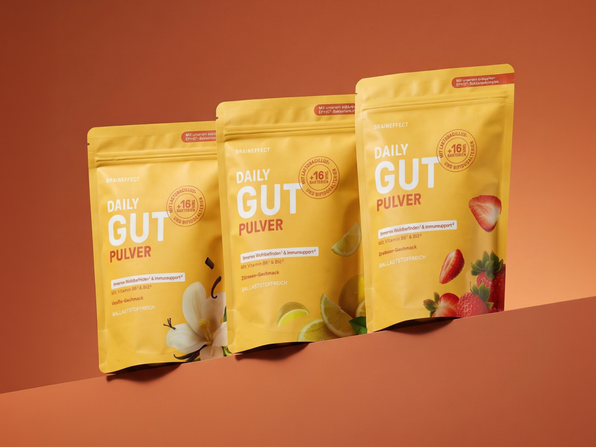 Drei gelbe Standbodenbeutel von BRAINEFFECT mit den Aufschriften "BRAINEFFECT DAILY GUT PULVER", "Inneres Wohlbefinden¹ & Immunsupport²", "MIT Vitamin B6¹ & B12²", "BALLASTSTOFFREICH" auf braunem Hintergrund.