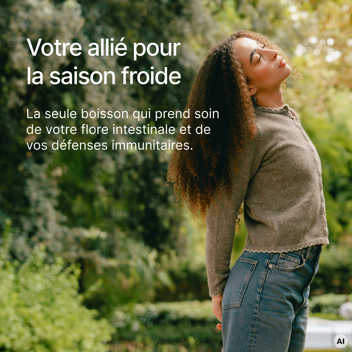 Une jeune femme aux cheveux bouclés se tient en plein air devant de la verdure, avec le texte "Votre allié pour la saison froide" et "La seule boisson qui prend soin de votre flore intestinale et de vos défenses immunitaires."