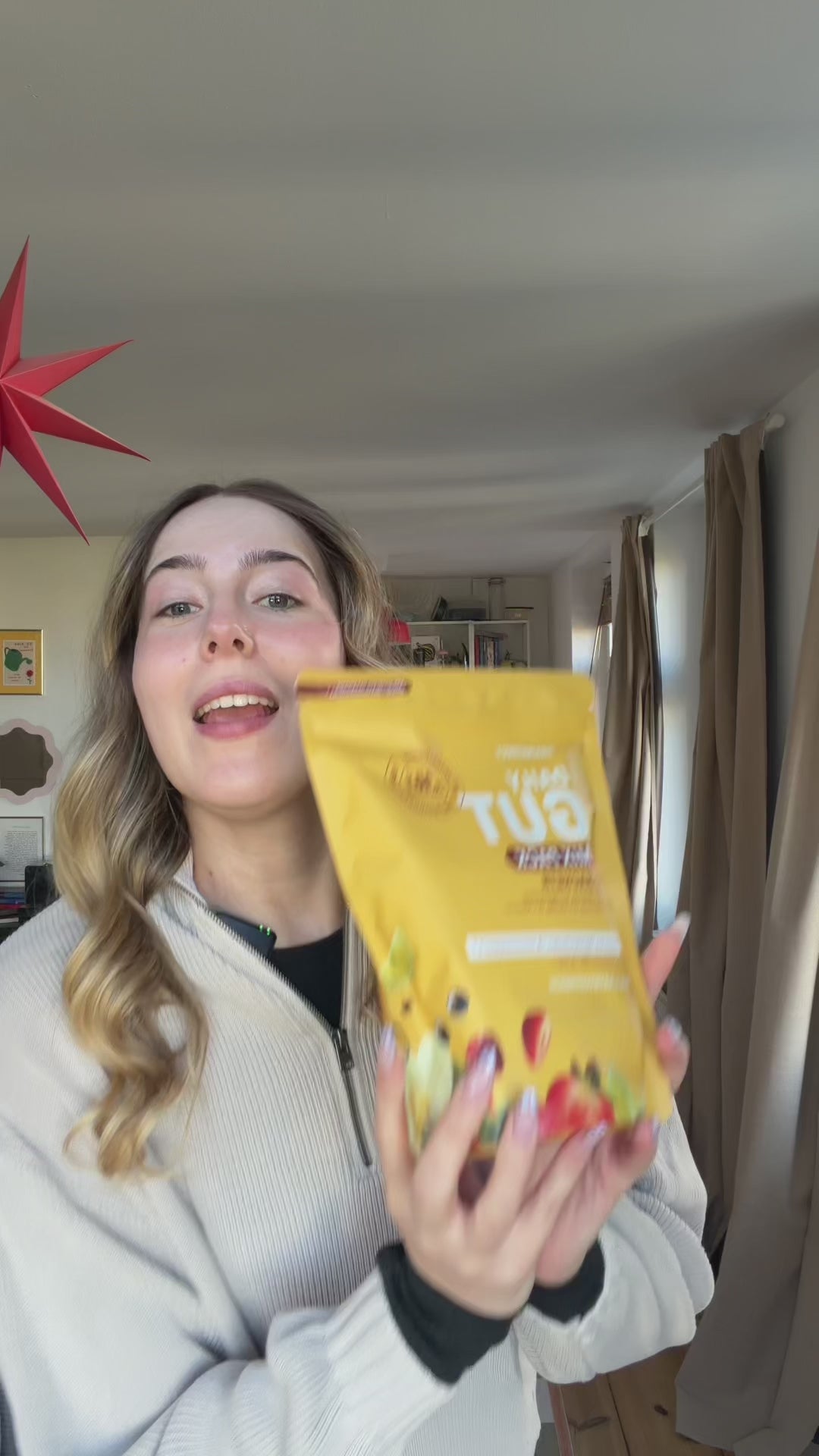 Load video: Eine Frau in einem hellen Pullover hält eine gelbe BRAINEFFECT-Produktverpackung mit der Aufschrift "DAILY GUT" in die Kamera.