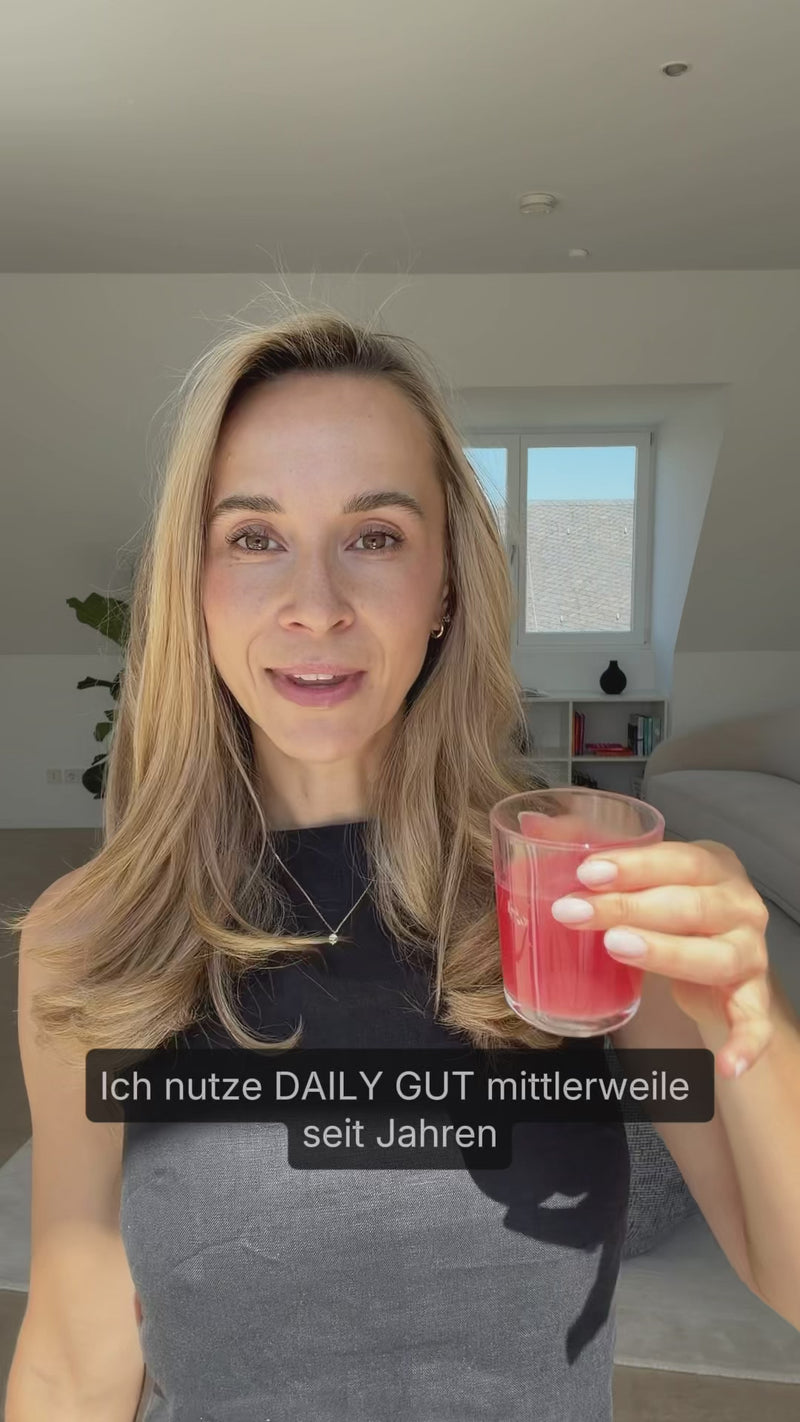 Eine blonde Frau hält ein Glas mit rötlicher Flüssigkeit in den Händen und sagt im Video: "Ich nutze DAILY GUT mittlerweile seit Jahren"